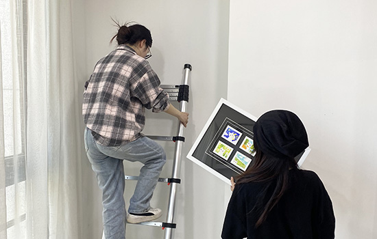 Zwei Mädchen benutzen eine EN131 Teleskopleiter, um ein Gemälde aufzuhängen