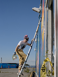 Ein Mädchen klettert auf eine Teleskopleiter, um die Wand zu streichen